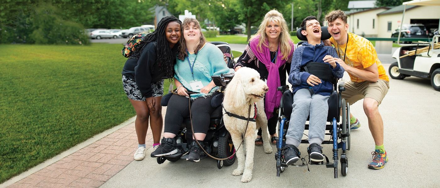 Volunteers and guests, several in wheelchairs, smiling together with a dog outside at a Joni and Friends Family Retreat.